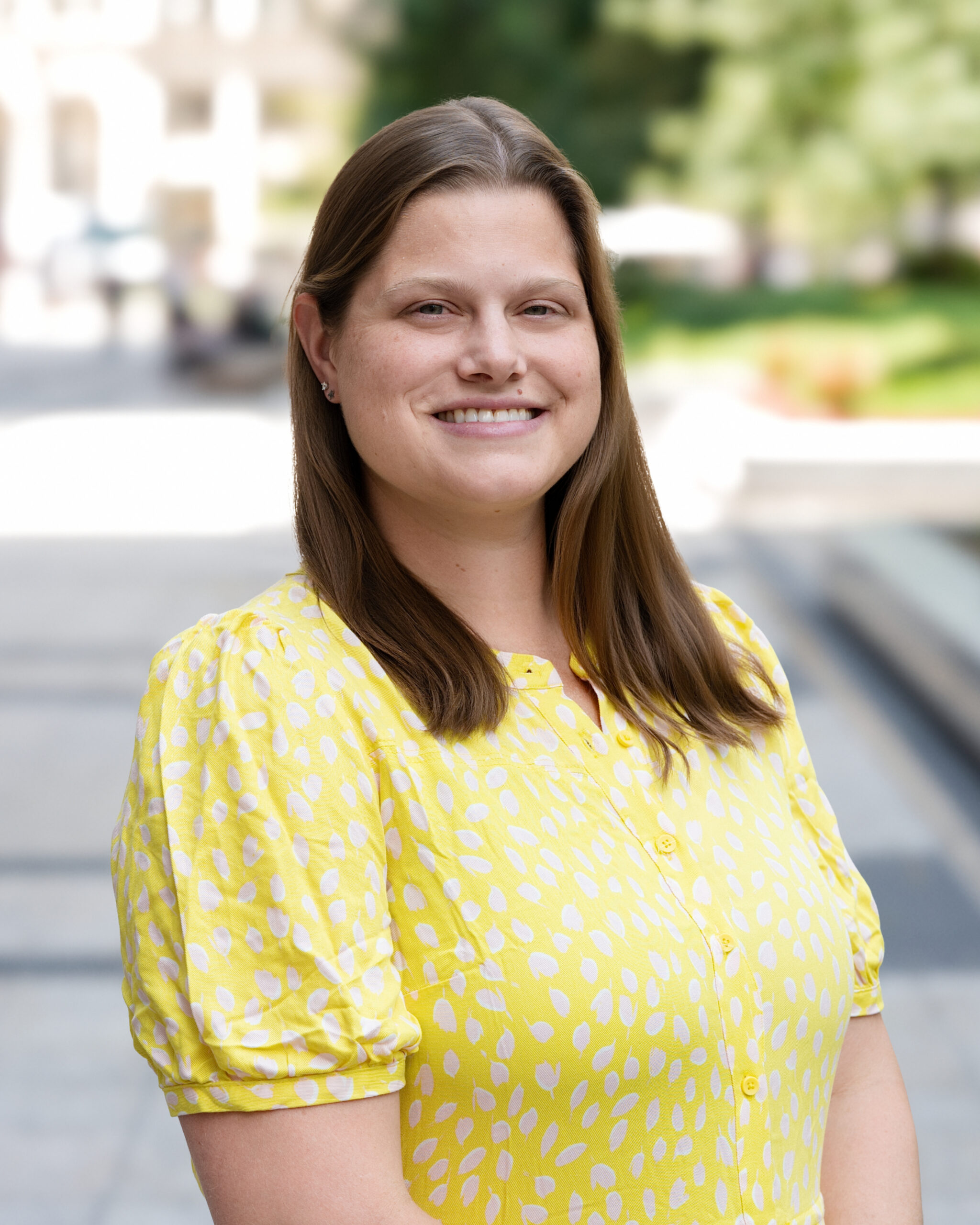 AWE-311-Jill - Alliance for Water Efficiency Smiling woman with long brown hair in a yellow polka-dot blouse outdoors.