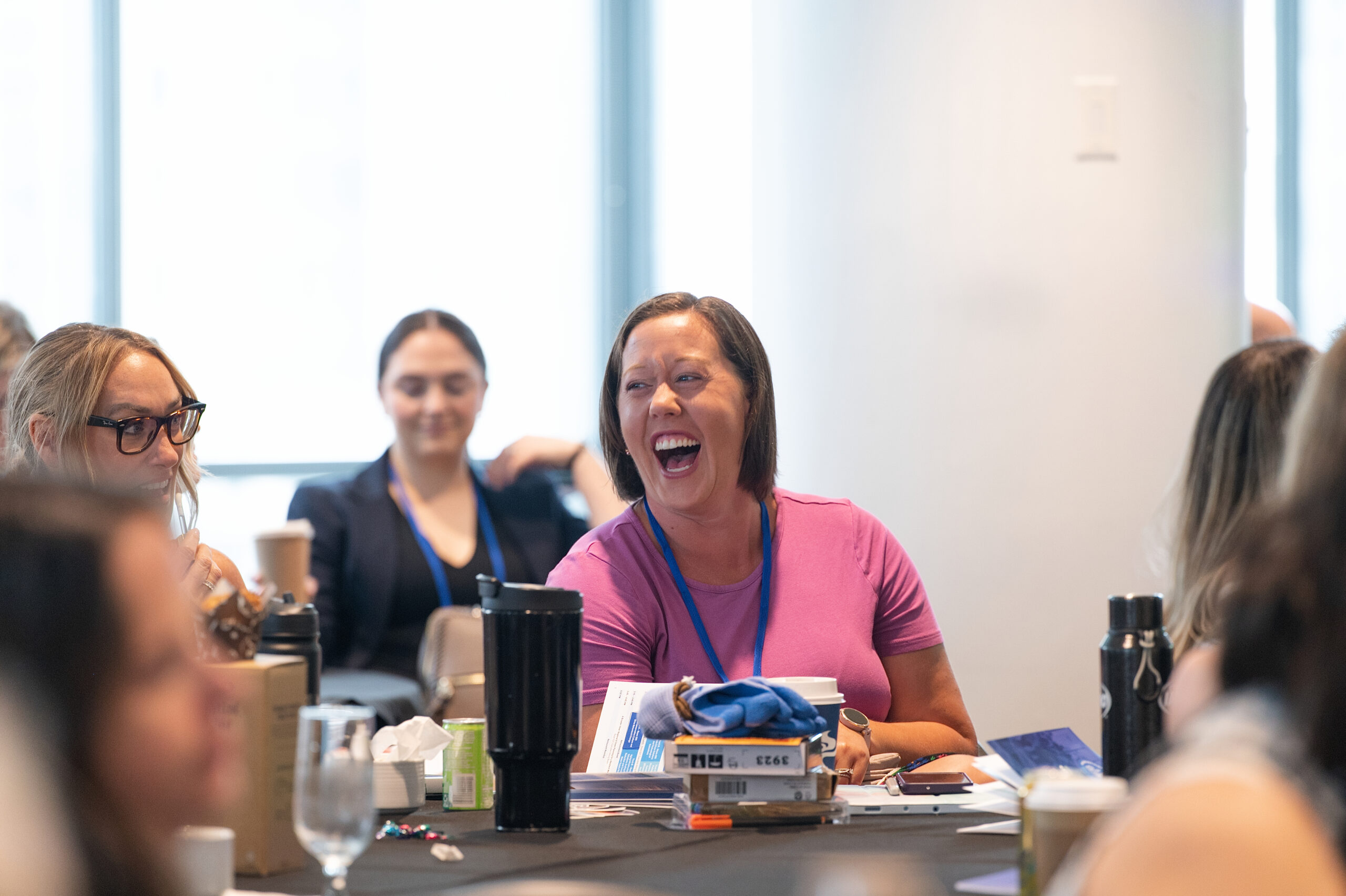 Group of professionals around a conference table, laughing and chatting during a meeting in a bright room.
