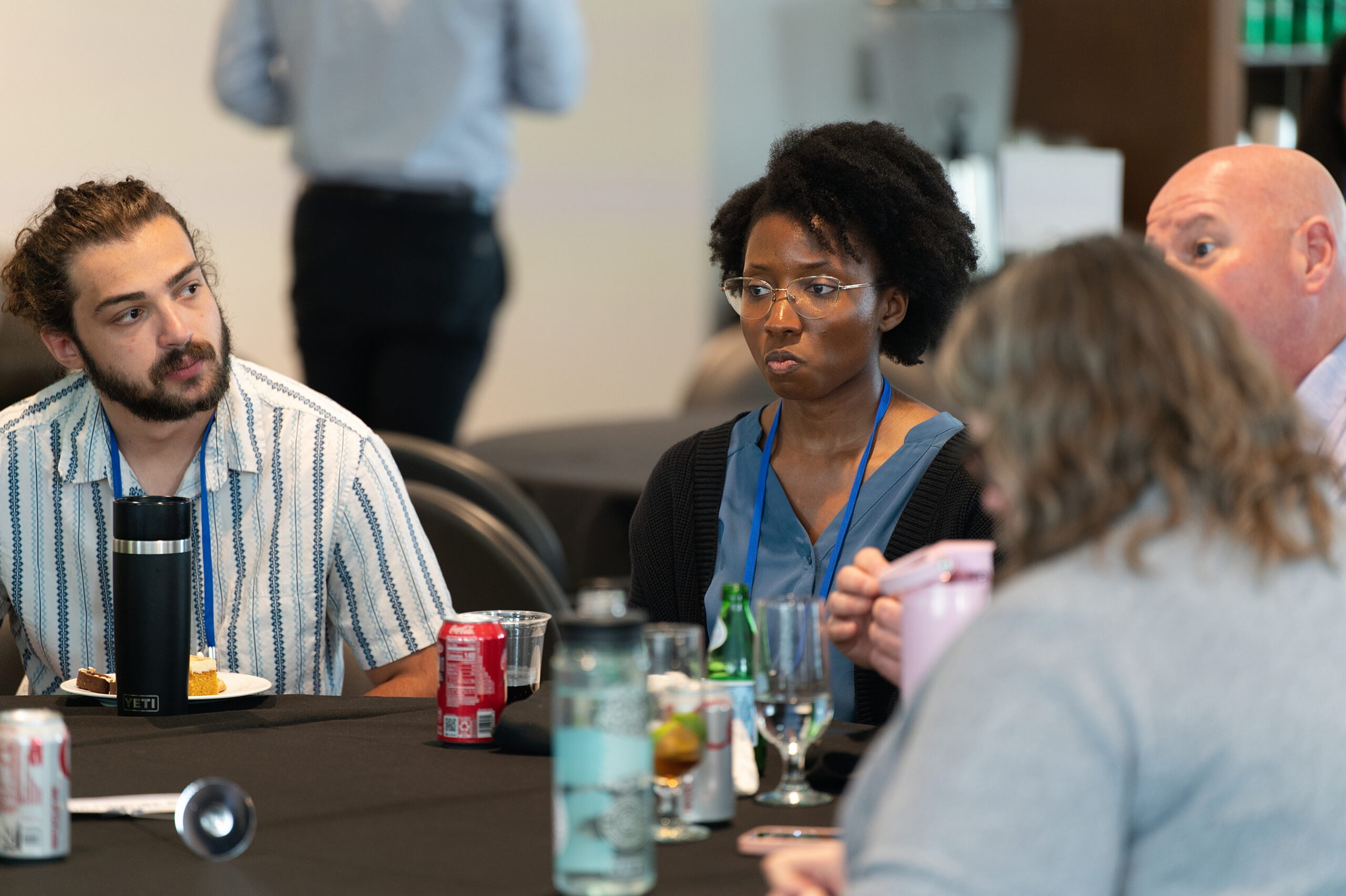 Group of people seated around a table with drinks, snacks, and conversation in a meeting or social setting.